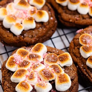 A close up of a hot chocolate cookie on a cooling rack after being topped with toasted marshmallows and crushed candy canes.