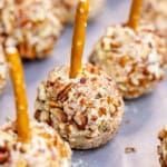 Mini cheese ball bites on a baking sheet with a pretzel stick in the top.