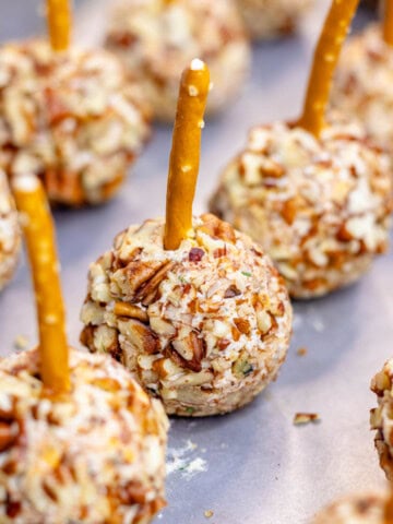 Mini cheese ball bites on a baking sheet with a pretzel stick in the top.