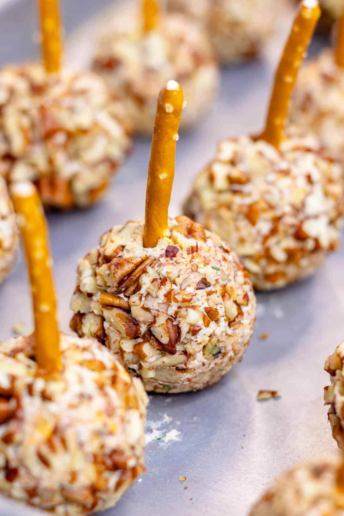Mini cheese ball bites on a baking sheet with a pretzel stick in the top.