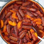 Sweet and sour sausages in a white cast iron pan after baking with a silver serving spoon.