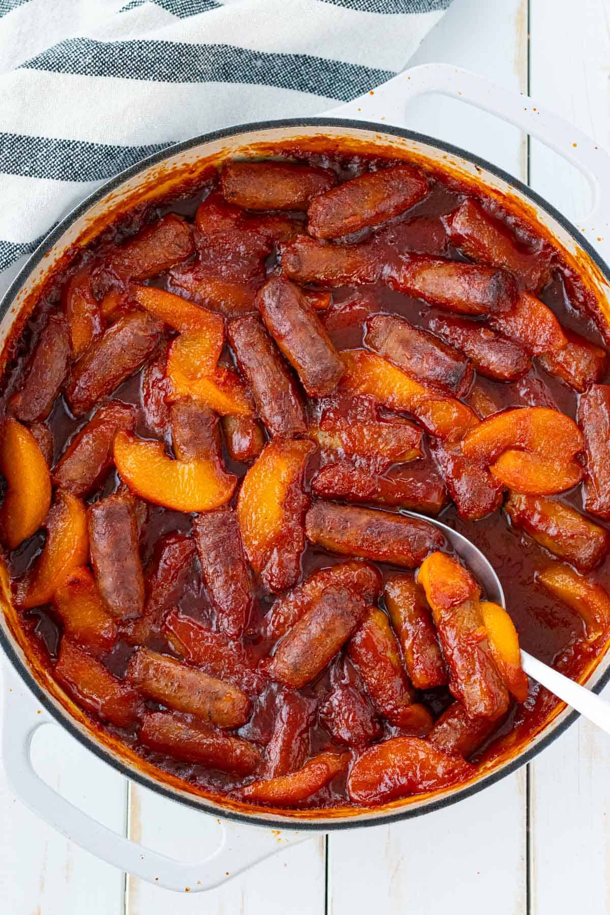 Sweet and sour sausages in a white cast iron pan after baking with a silver serving spoon.