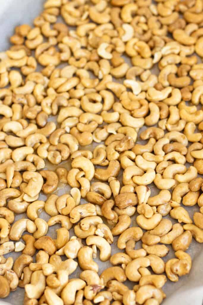 Cashews coated in honey butter on a baking sheet lined with parchment paper.