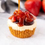 Drizzling caramel sauce on top of a single strawberry nutella cheesecake cupcake.