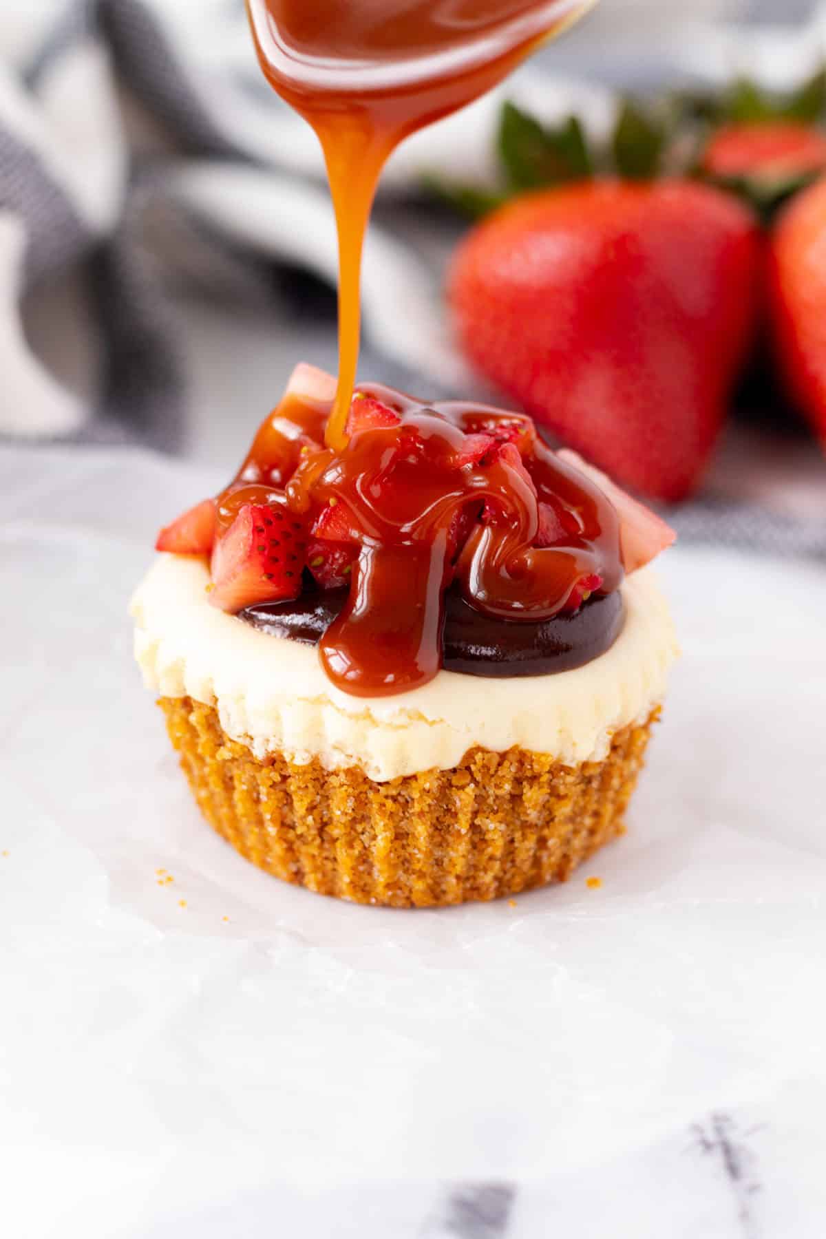Drizzling caramel sauce on top of a single strawberry nutella cheesecake cupcake.