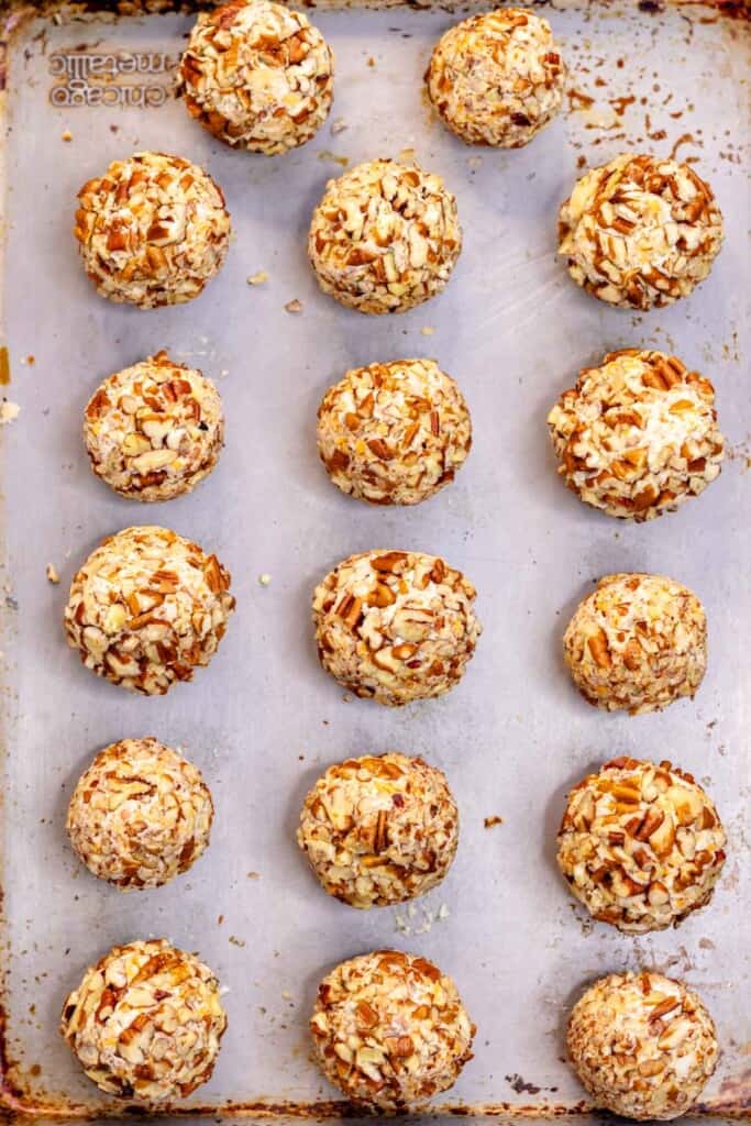 Mini cheese balls on a baking sheet, rolled in crushed pecans.