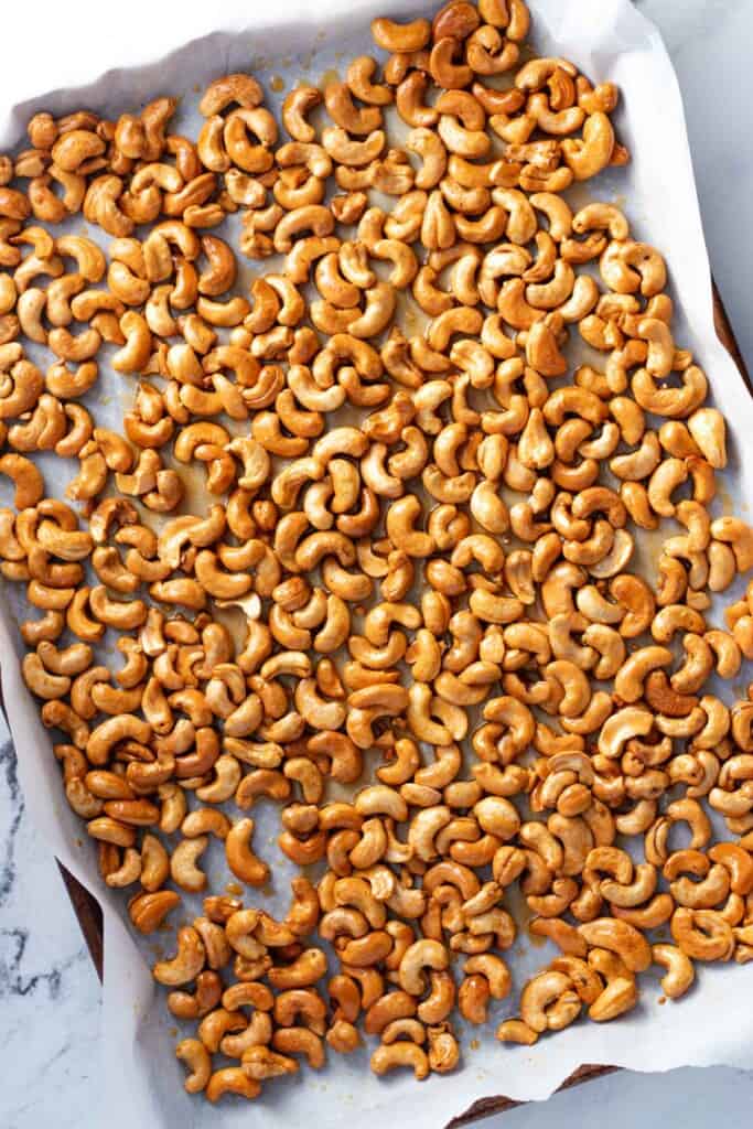 Cashews spread out on a baking sheet after they have been roasted with honey butter.