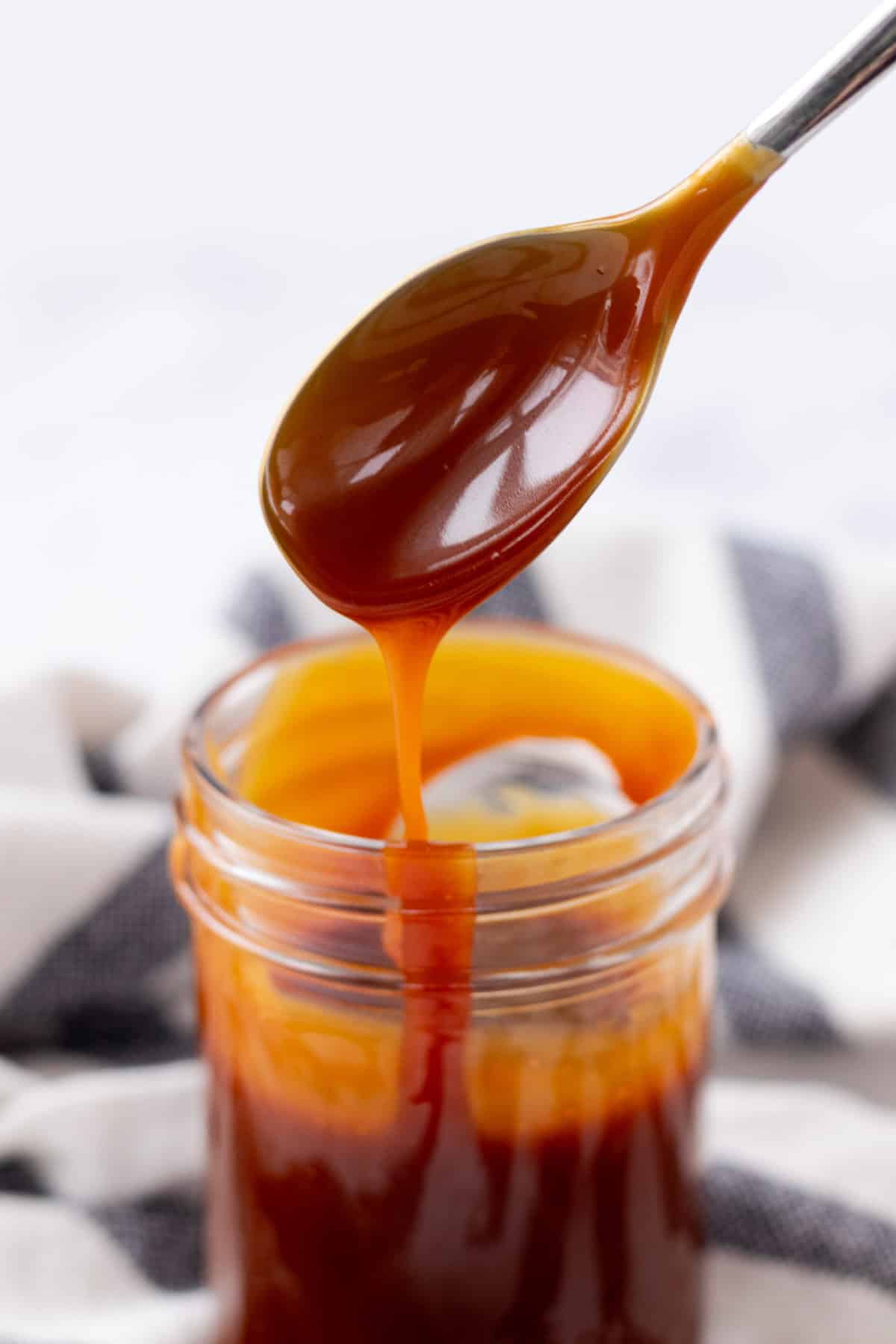 Caramel sauce dripping off of a spoon to show the consistency.
