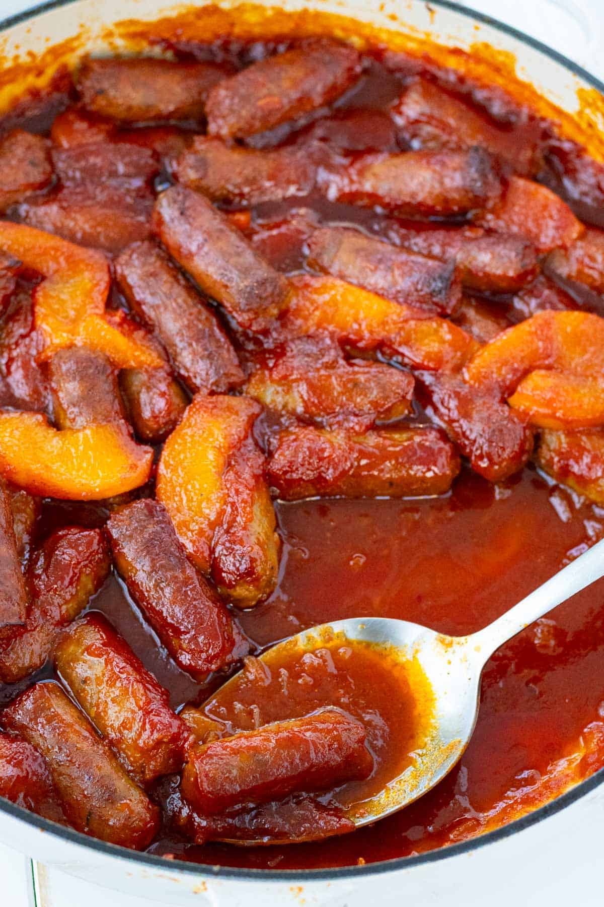 A sliver spoon serving sweet and sour sausages.