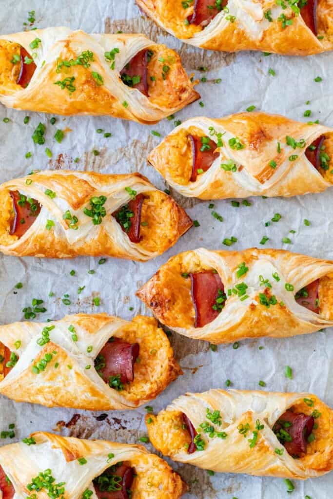 Ham and cheese croissants on a baking sheet sprinkled with chives.