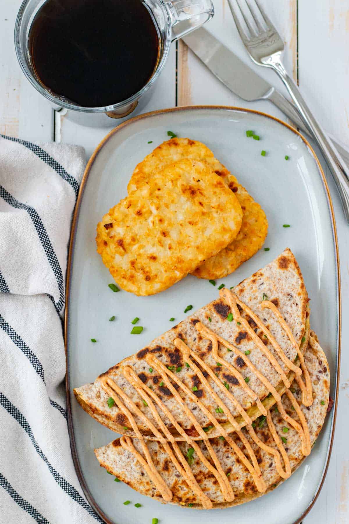A plate of two breakfast tacos, drizzled with sriracha aioli and a side of hash browns.