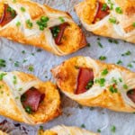 Baked ham and cheese croissants on a baking sheet with parchment paper, topped with fresh chives.