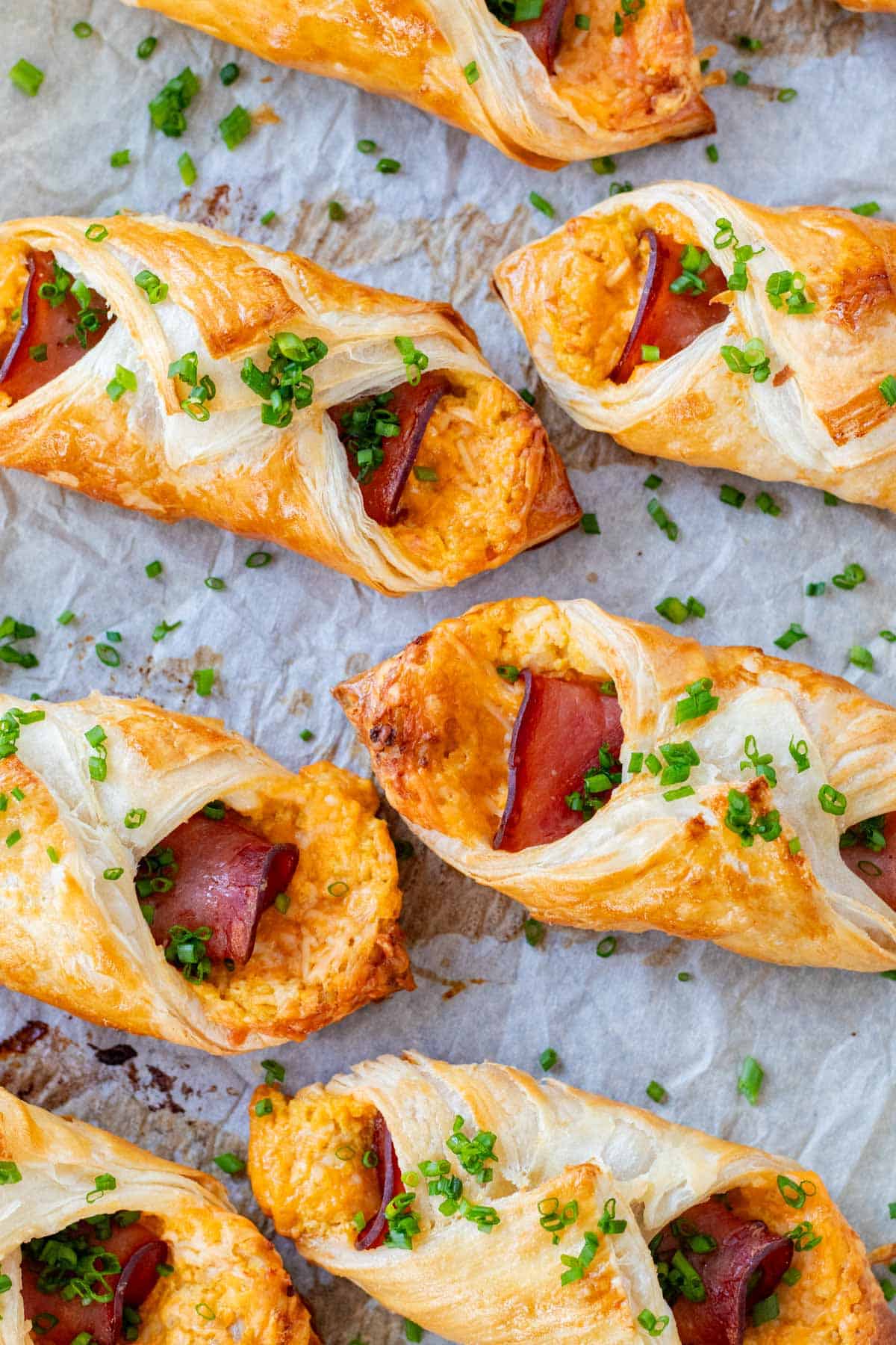 Baked ham and cheese croissants on a baking sheet with parchment paper, topped with fresh chives.