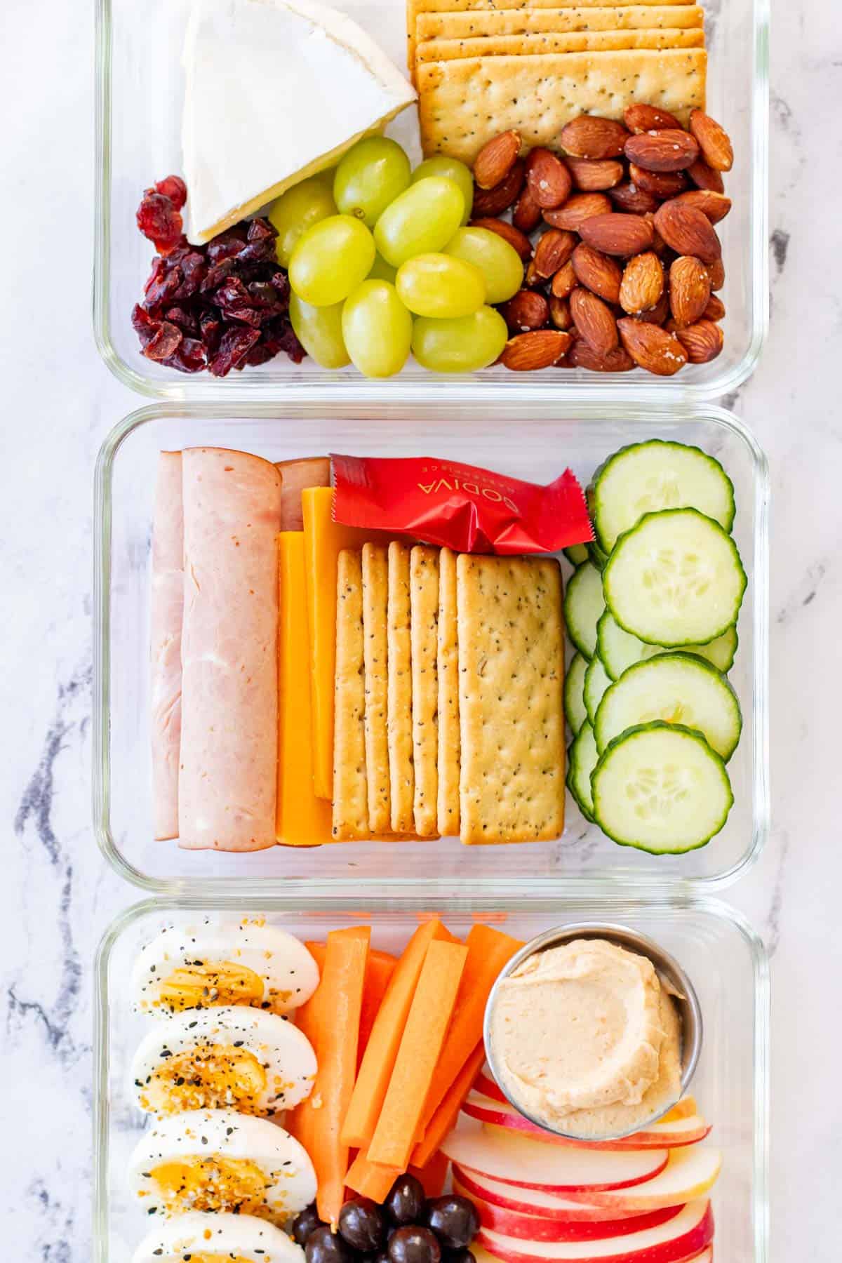 Three adult lunchable options in a row. Ham and cheese, brie and almond and, egg and apple.
