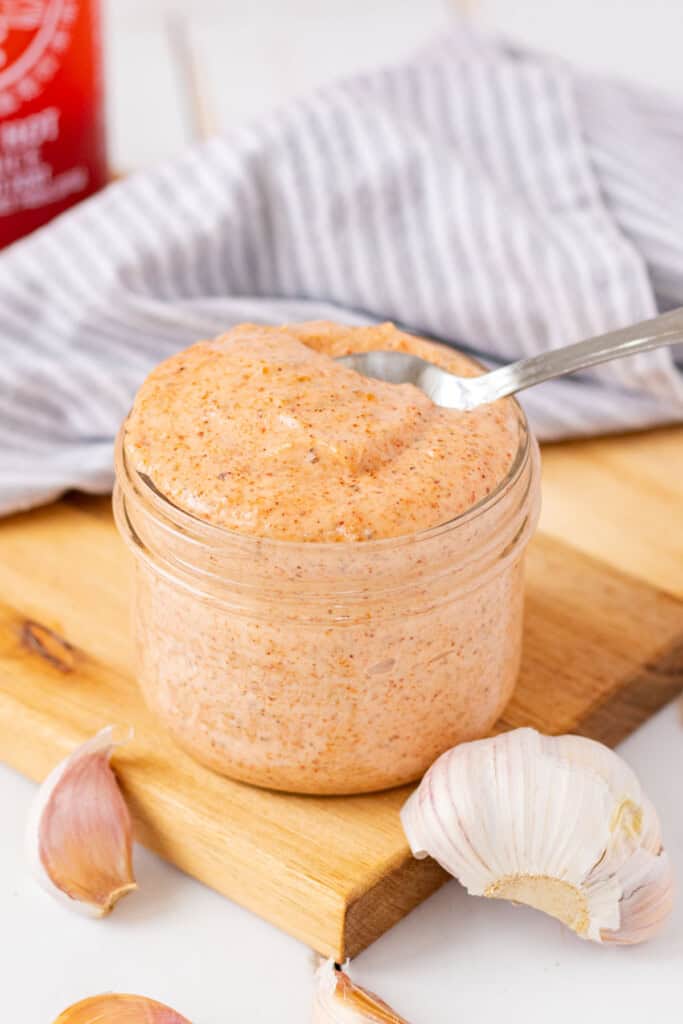 A jar filled with sriracha ailoi with a spoon in it.
