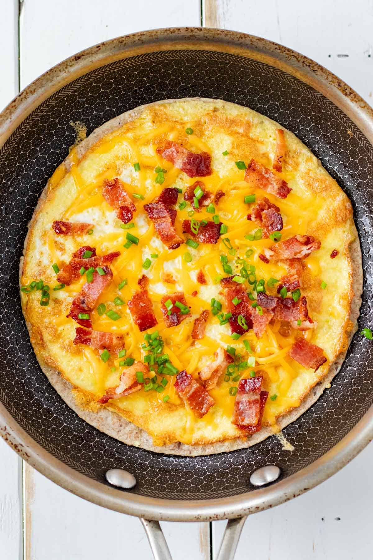 Flipping the breakfast taco and adding bacon, chives and more cheese to the other side.