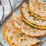 Breakfast tacos lined up on a blue serving plate with a bowl of sriracha aioli in the background.