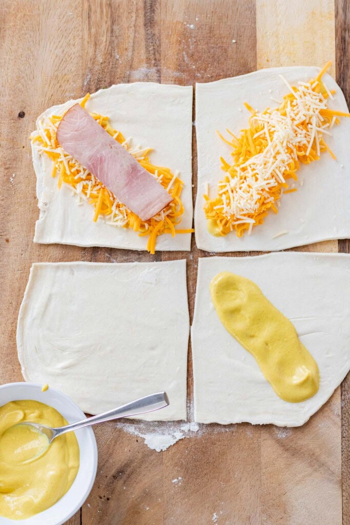 Building the croissants, one with dijon spread on the puff pastry, one topped with cheese and Parmesan, and the final one topped with ham.