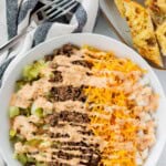 A large big mac salad in a white bowl with garlic bread baguette on the side.