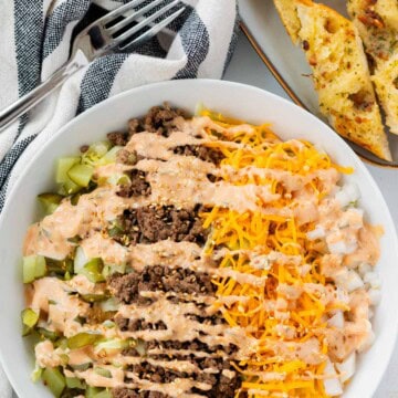 A large big mac salad in a white bowl with garlic bread baguette on the side.