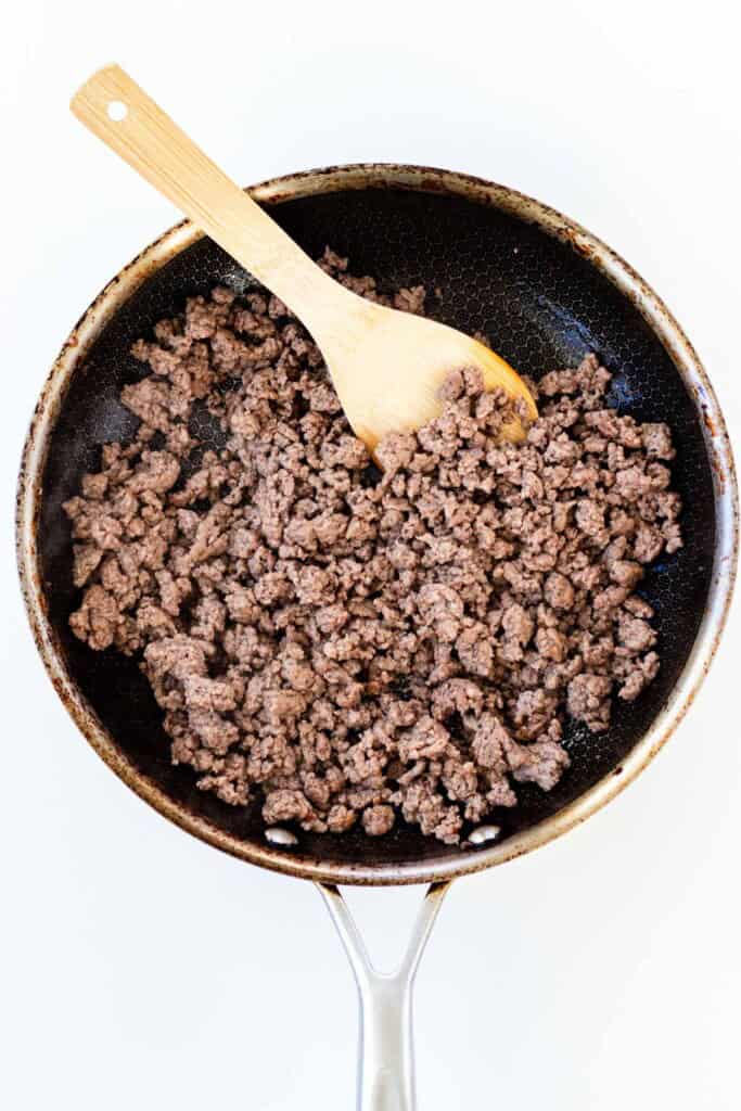 A frying pan with browned ground beef in it.