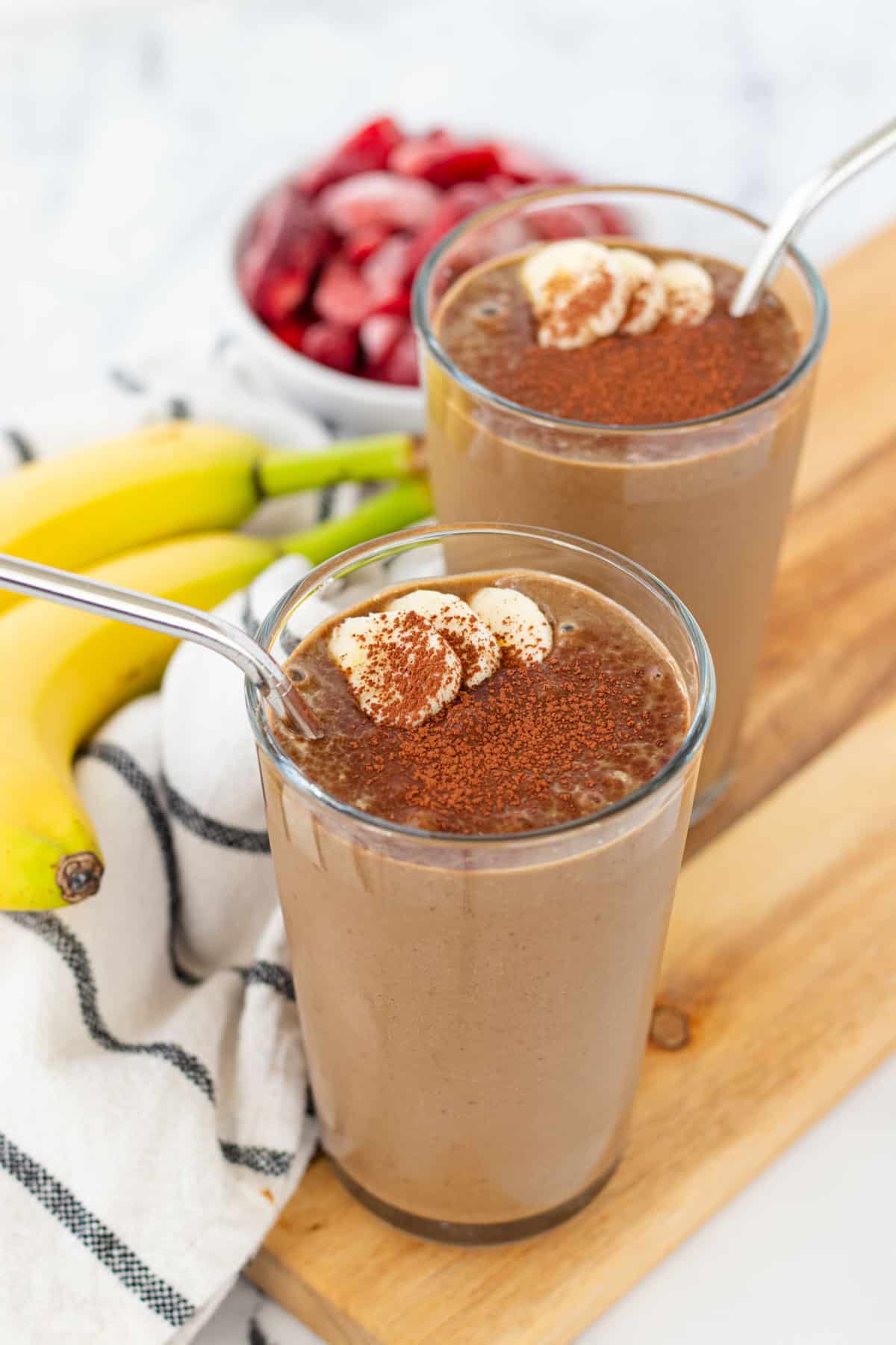 Chocolate peanut butter banana smoothies in two glasses, sprinkled with cocoa powder and topped with extra sliced bananas.