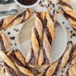 Two chocolate twist pastries on a plate with more chocolate twists surrounding the plate.