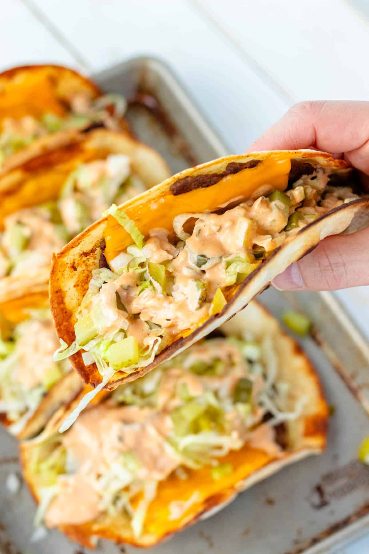 Holding a smash burger taco stuffed with big mac ingredients.