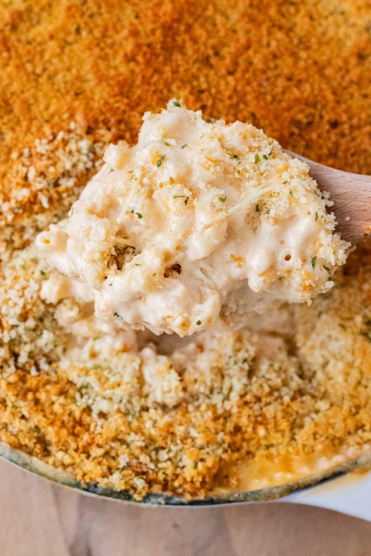 Using a wooden spoon to take a big scoop of creamy mac and cheese.