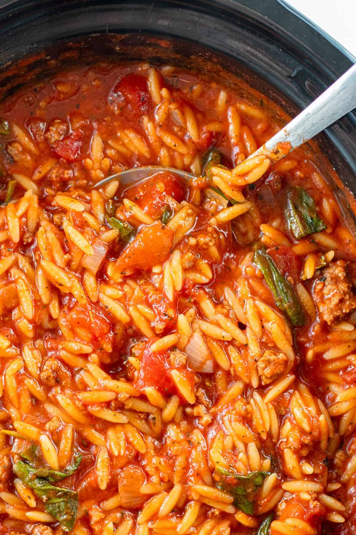 A silver serving spoon scooping lasagna soup out of a slow cooker.