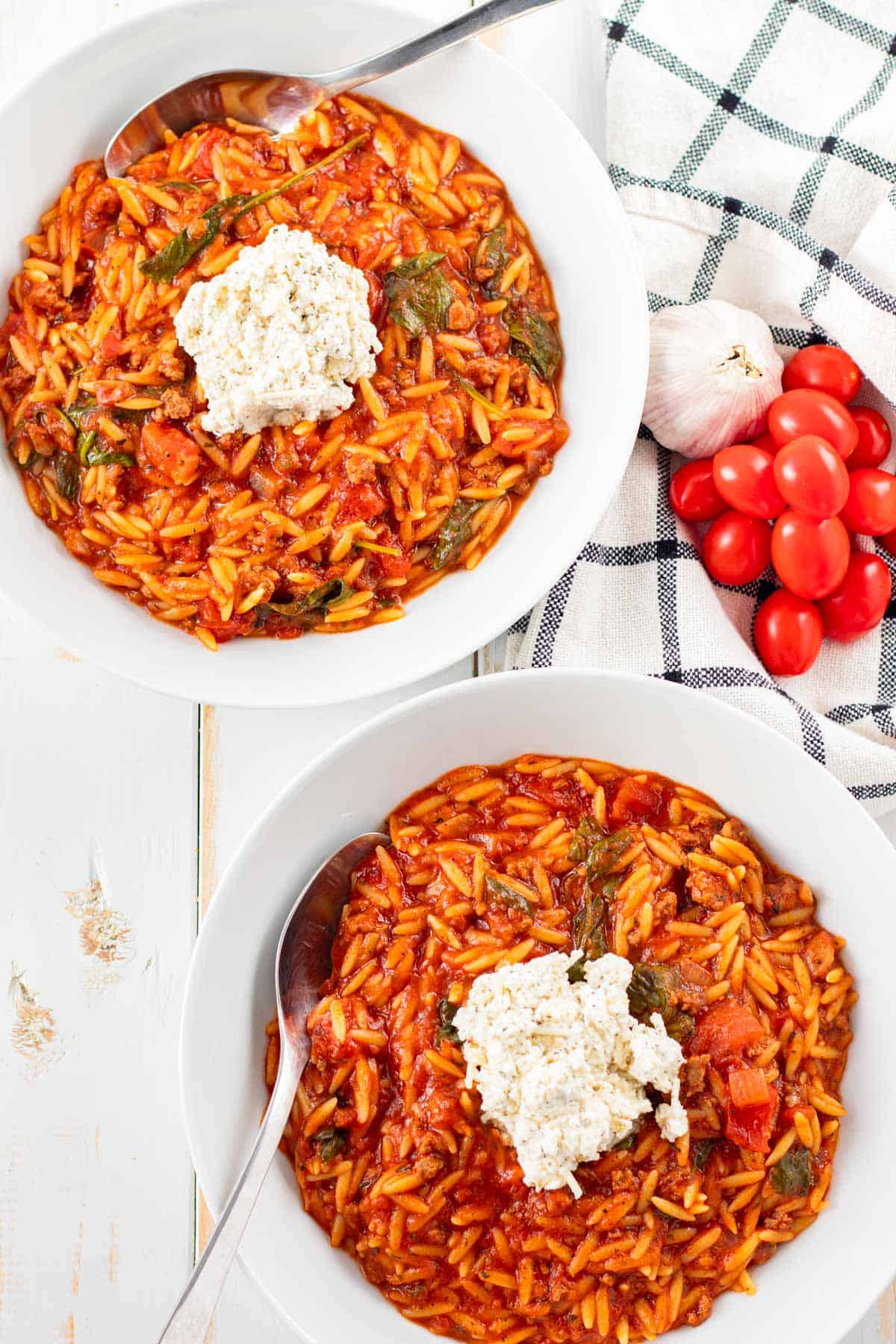 Two large bowls filled with lasagna soup and topped with a dollop of spiced ricotta topping.