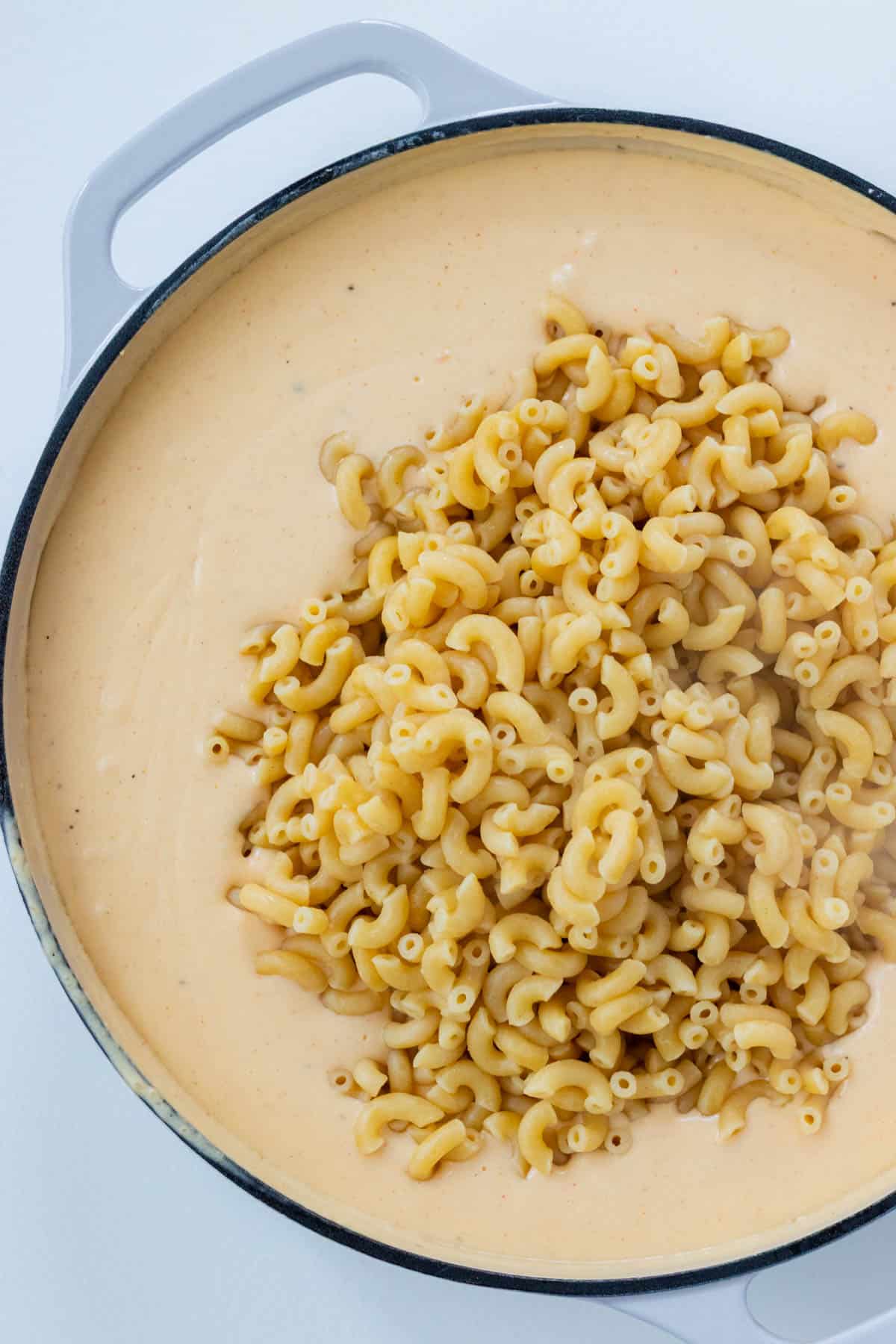 Stirring the cooked elbow noodles into the gouda cheese sauce.