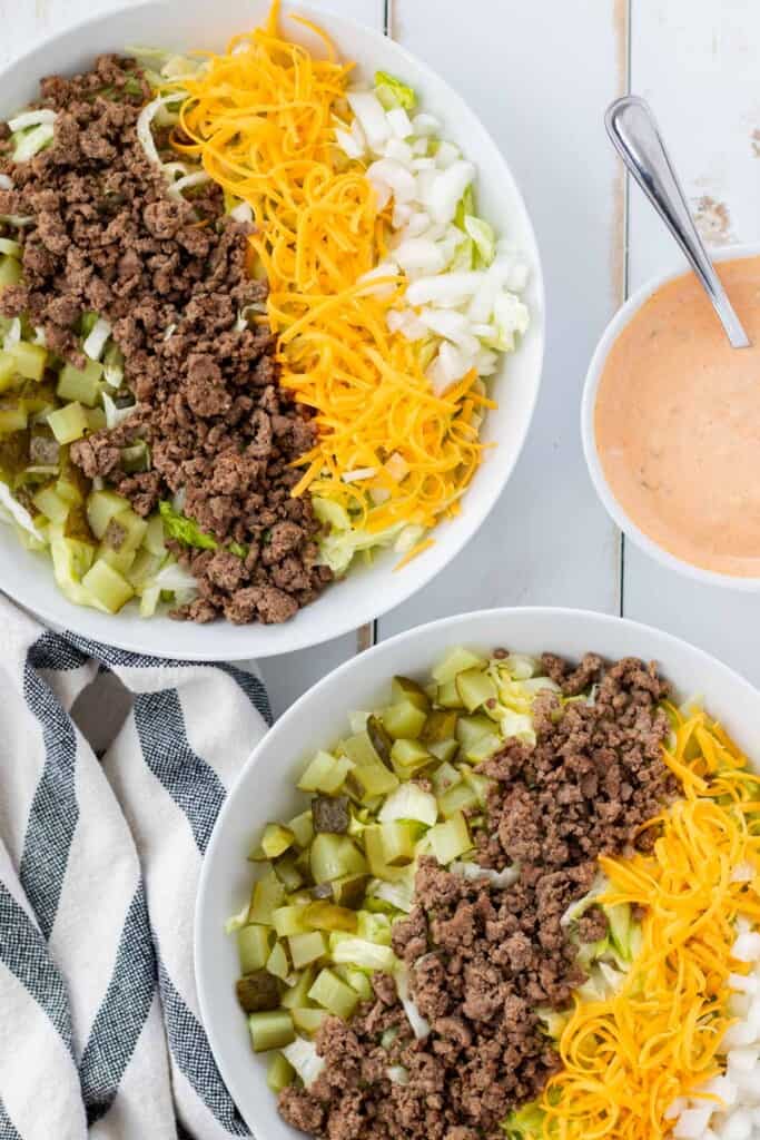 Building the salads by adding the pickles, onions, ground beef, and cheddar cheese.