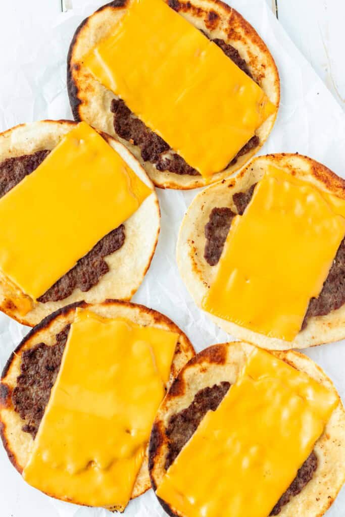 Cooked smash burger tacos with cheese melted on top.