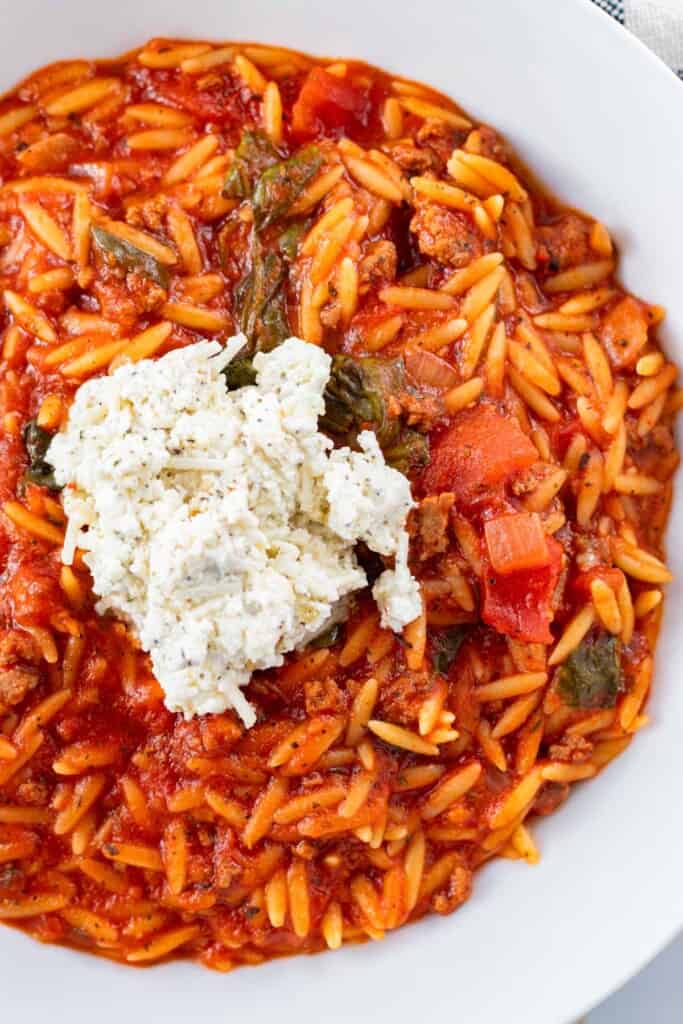 Adding a dollop of spiced ricotta cheese on top of a bowl of lasagna soup.