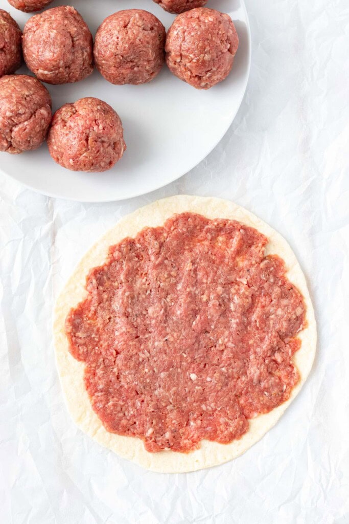 Pressing the ground beef mixture onto flour tortillas.