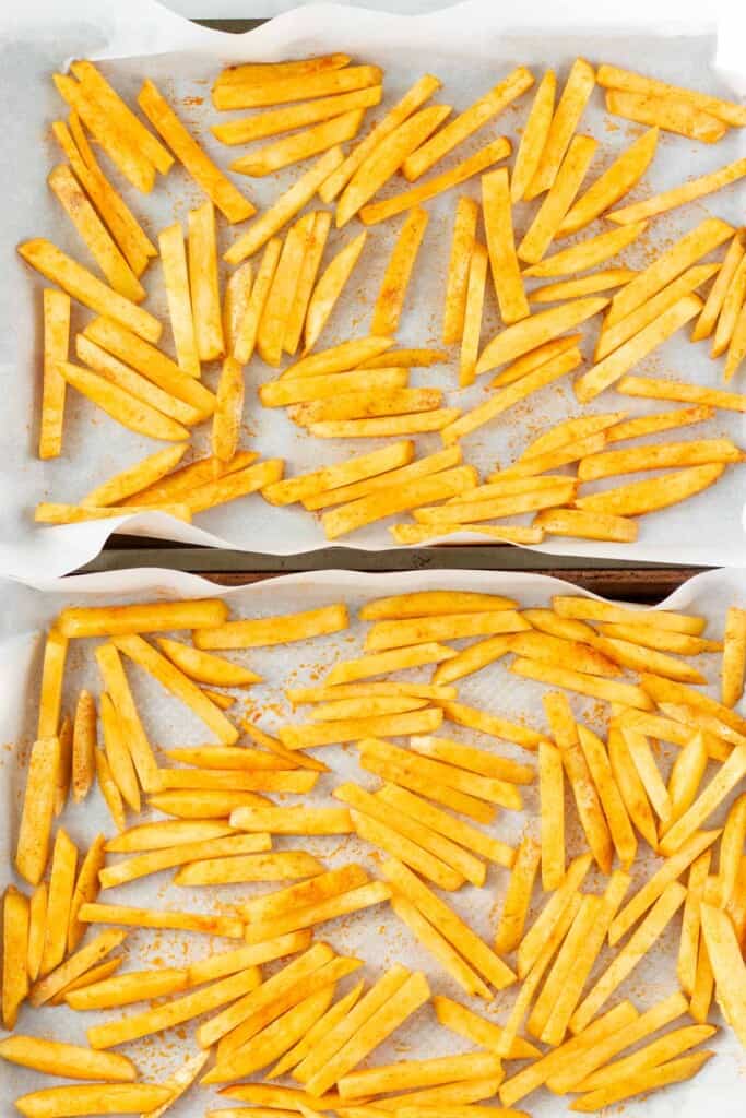 Adding the oil and spices and spreading the fries on parchment lined baking sheets.