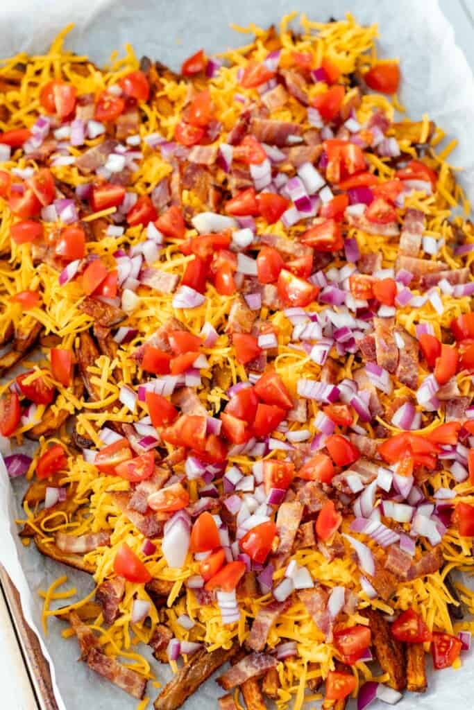 Layering all the toppings on top of the fries on a baking sheet.