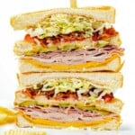 A club sandwich cut in half, stacked on top of one another with chips scattered in the background.