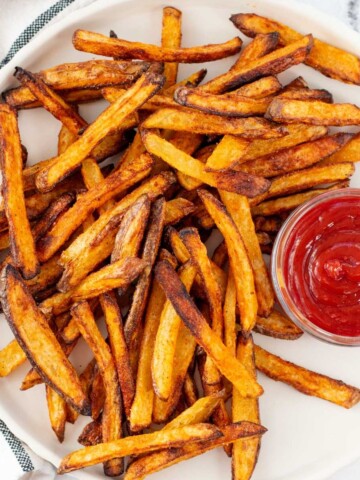 A plate full of crispy golden oven baked french fries with a side of ketchup.
