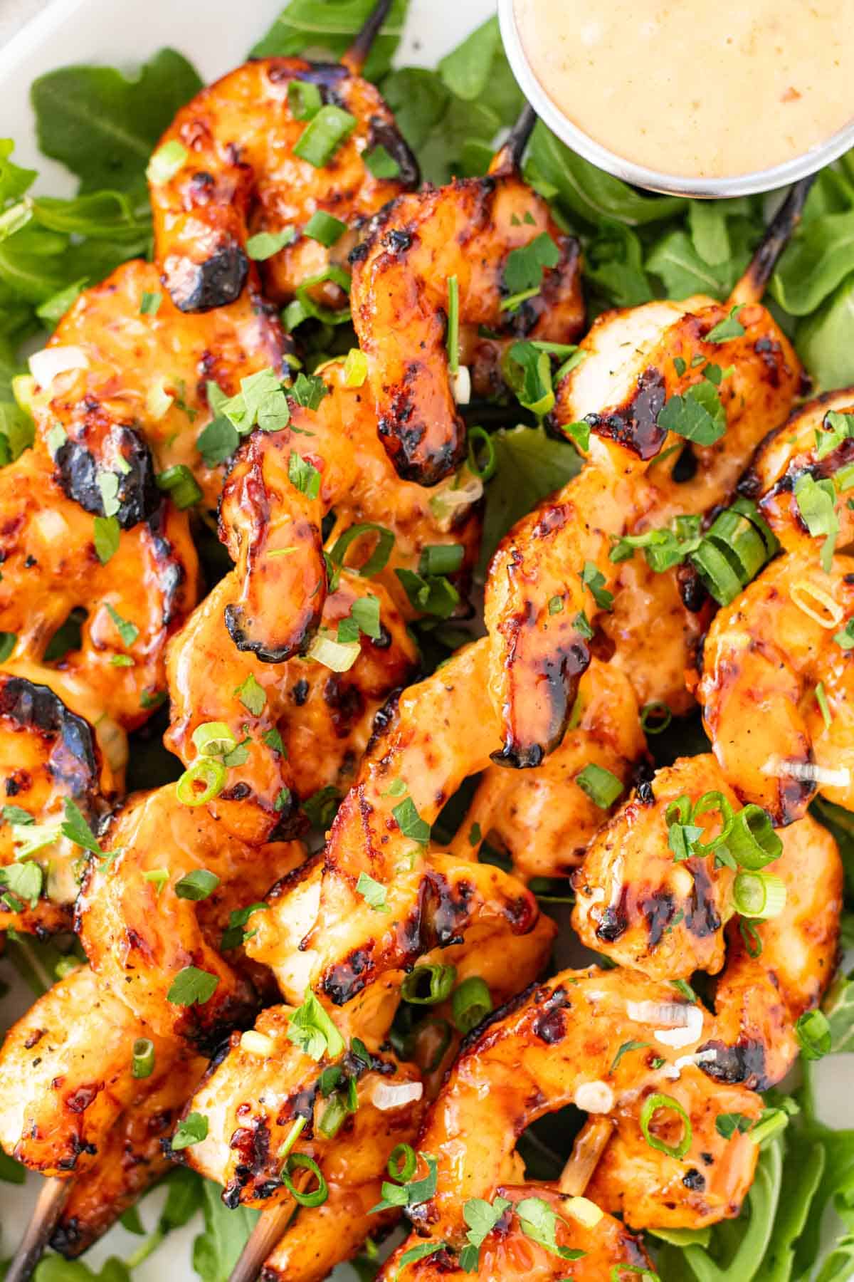 Grilled shrimp on skewers coated in bang bang sauce on a serving dish with arugula.