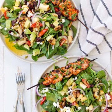 Two plates of harvest salad with shrimp skewers on the side.