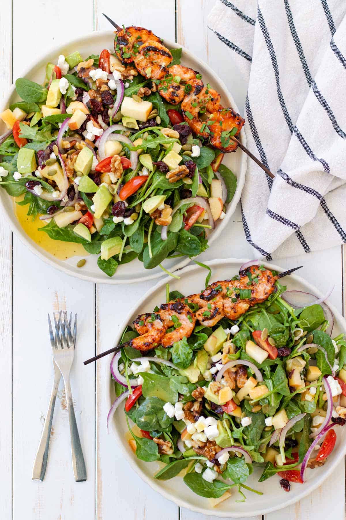 Two plates of harvest salad with shrimp skewers on the side.