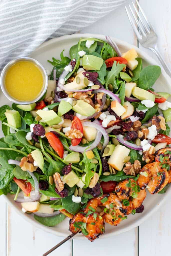 A single serving plate of salad with a shrimp skewer and dressing on the side.