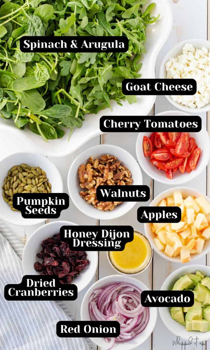 Ingredients include spinach, arugula, goat cheese, cherry tomatoes, walnuts, pumpkin seeds, dried cranberries, apples, red onion, avocado and honey dijon vinaigrette dressing.
