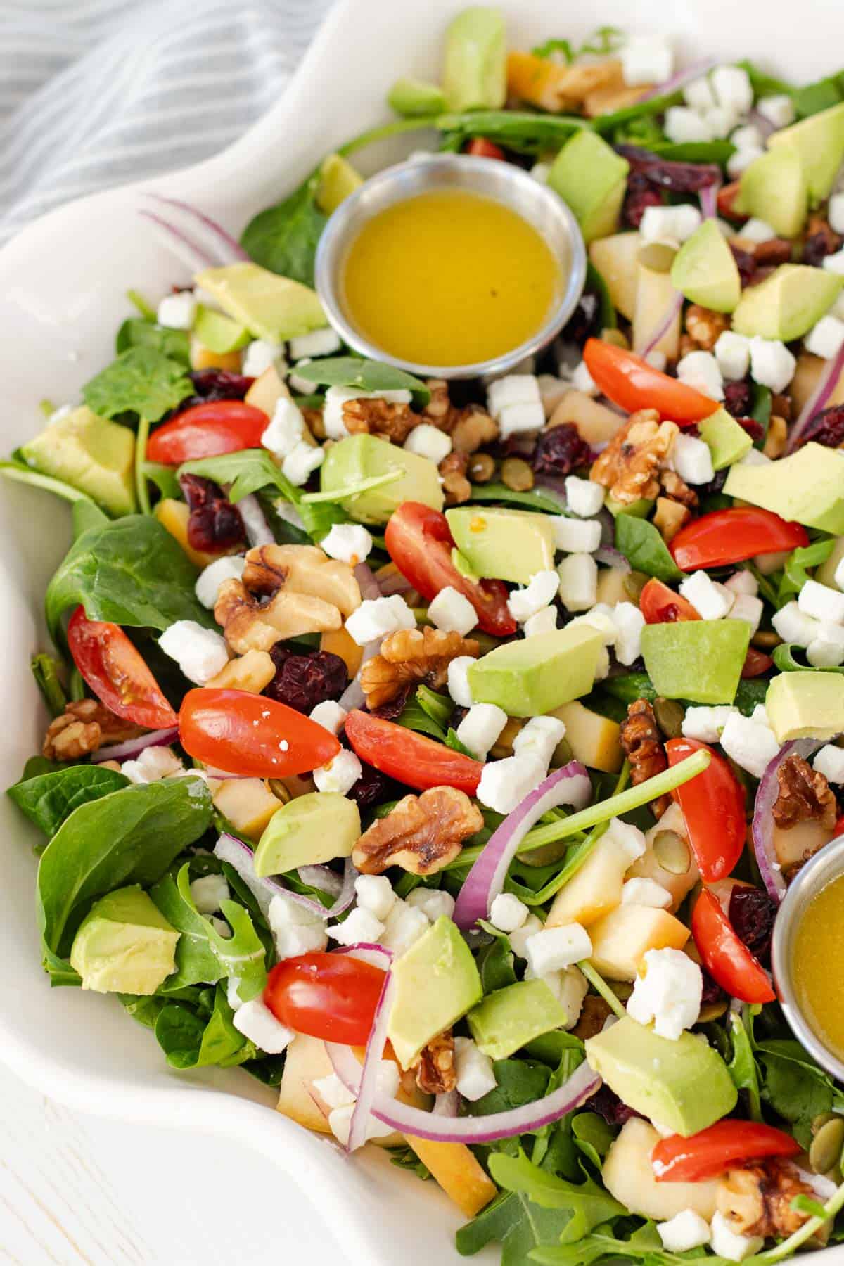 Harvest salad in a large white serving bowl with a pot of dressing nestled into the salad.