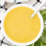 A bowl full of honey dijon salad dressing and a spoon with arugula leaves on the side.