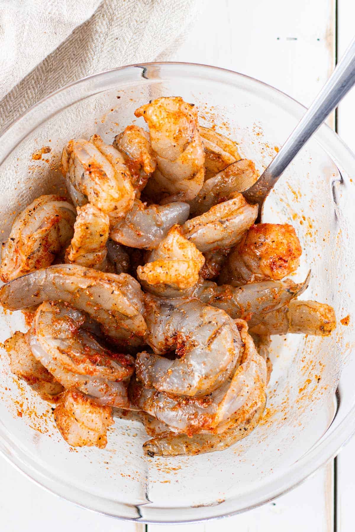Tossing the raw shrimp with avocado oil, lemon juice, and spices in a bowl.