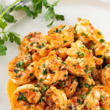 A pile of juicy garlic butter shrimp on a white plate.