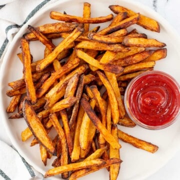 A plate of golden, crispy baked french fries with a side of ketchup on a marble background.